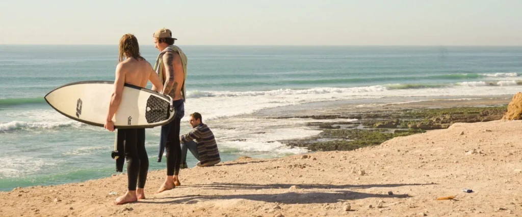 Three men watching the ocean surf breaks.